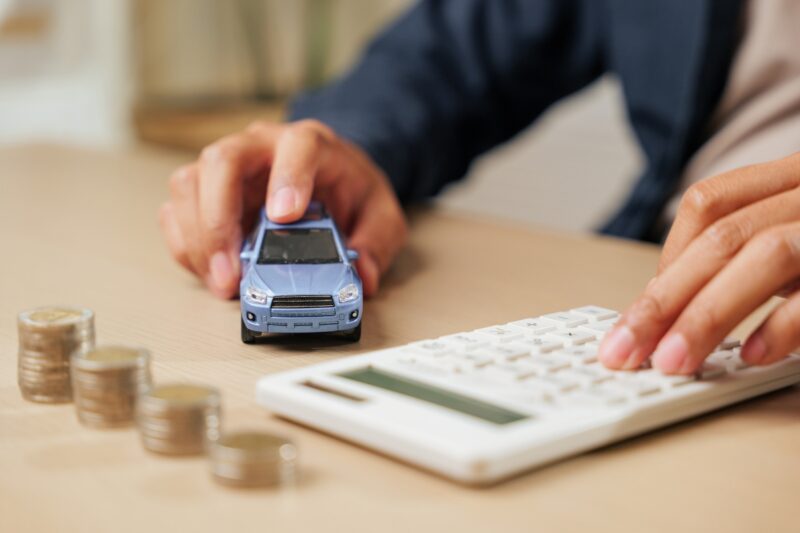 prikaz osobe koja drži u ruci kalkulator, automobil i novac u kovanicama pored na stolu