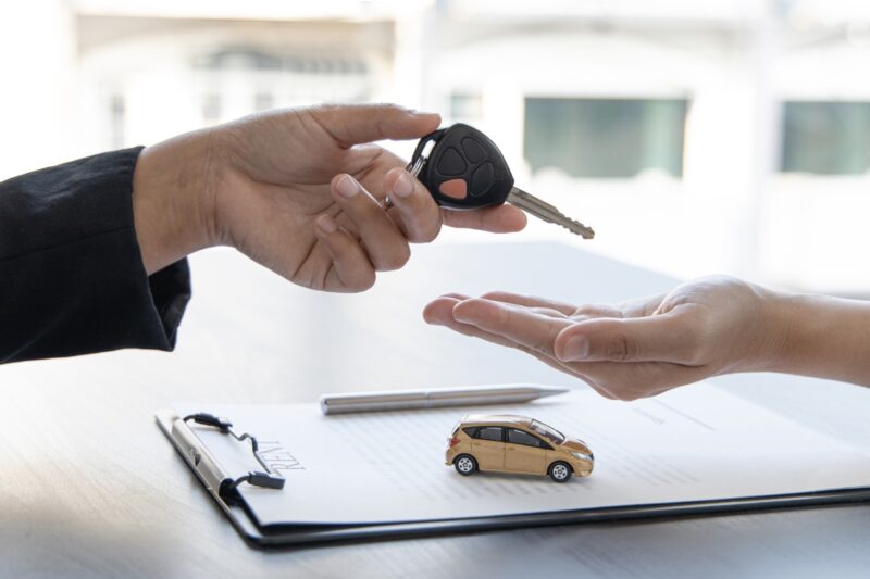 prikaz osobe koja predaje dokumentaciju i ključ od automobila drugoj osobi, na stolu je ta dokumentacija sa maketom automobila