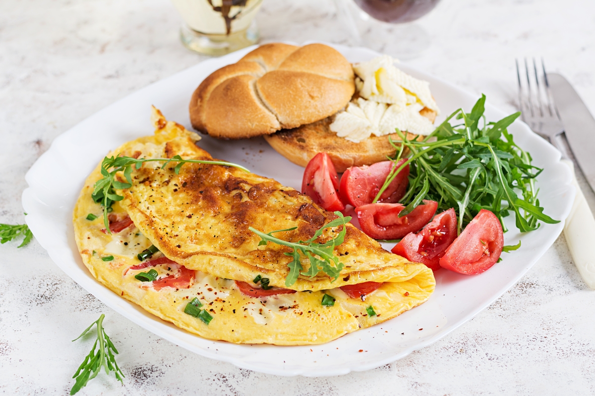 prikaz tanjira na kom je seviran omlet sa povrćem, salata od rukole i paradajza i parče hleba